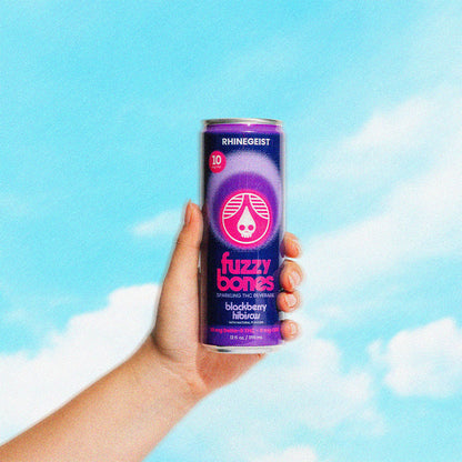 Hand holding a can of Fuzzy Bones blackberry hibiscus against a blue sky with clouds
